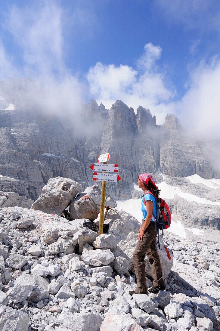 Frau blickt auf Wegweiser, Felswände im Hintergrund, Bocchetteweg, Brenta, Trentino-Südtirol, Italien