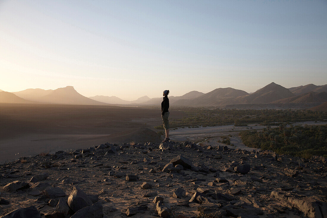 Woman standing on a rock looking at the sunset, Hartmann Valley, Namibia, Africa