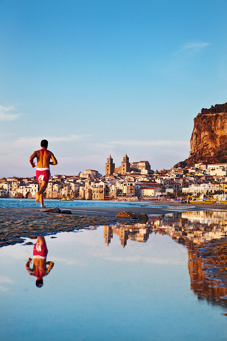 Jogger at beach,  old town, cathedral and cliff La Rocca, Cefalú, Palermo, Sicily, Italy