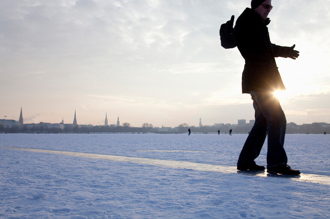 Mann schlittert auf gefrorener Außenalster im Winter, Hamburg, Deutschland