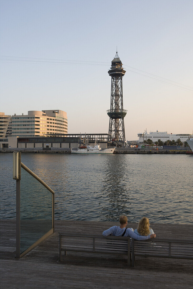 Couple on bench at harbor and Montjuic Teleferico cable car tower, Barcelona, Catalonia, Spain, Europe