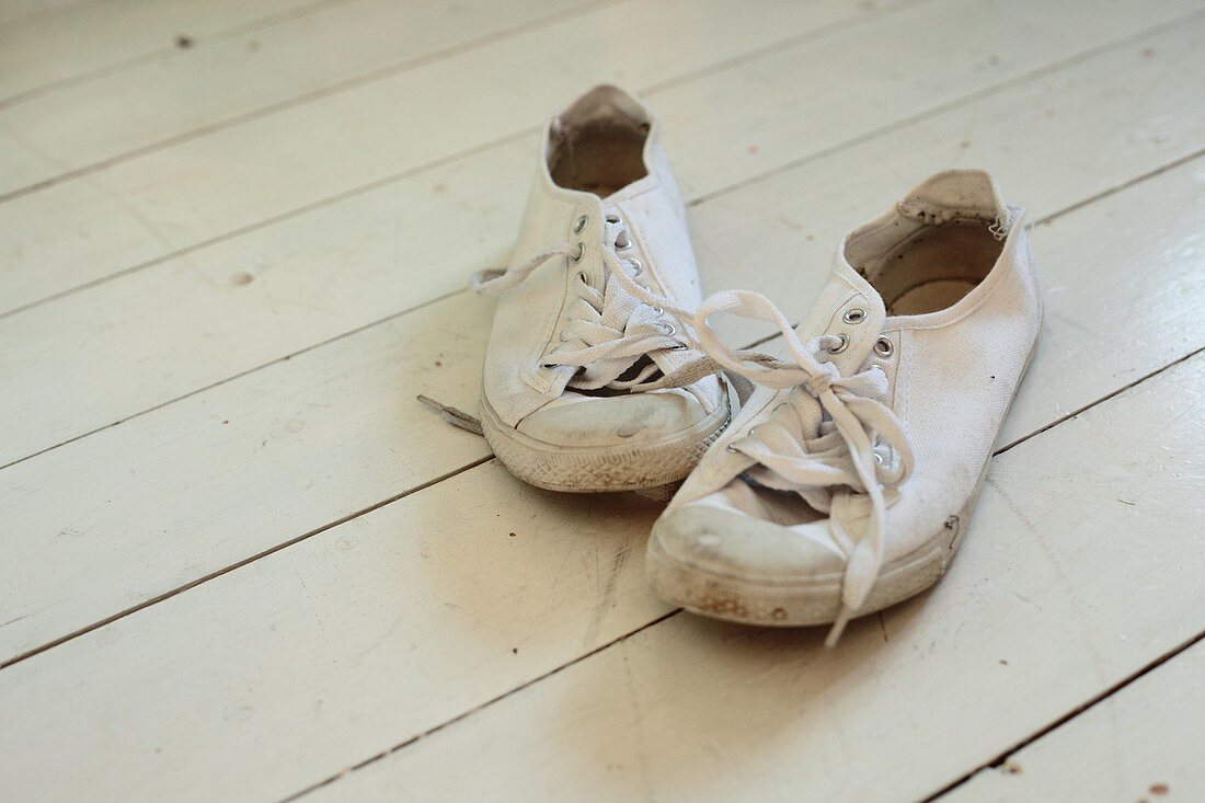 A pair of old plimsolls on a white wooden floor