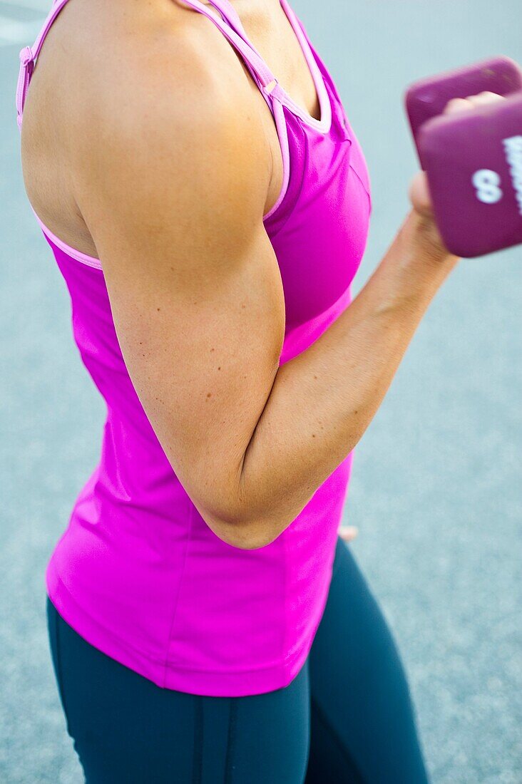 Close up of a thirty year old woman's flexed bi-cep pumping a dumbbell.