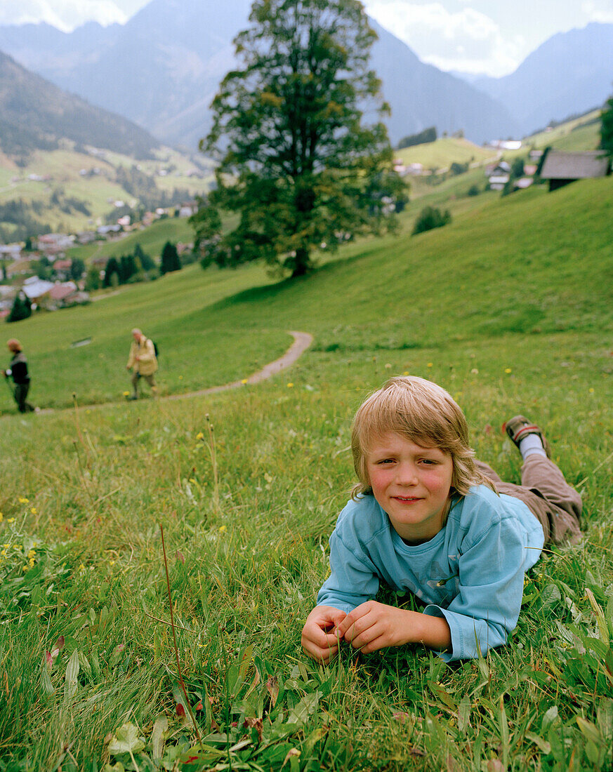 Boy lying in the meadow of an organic hotel, Hirschegg, Kleinwalsertal, Styria, Austria
