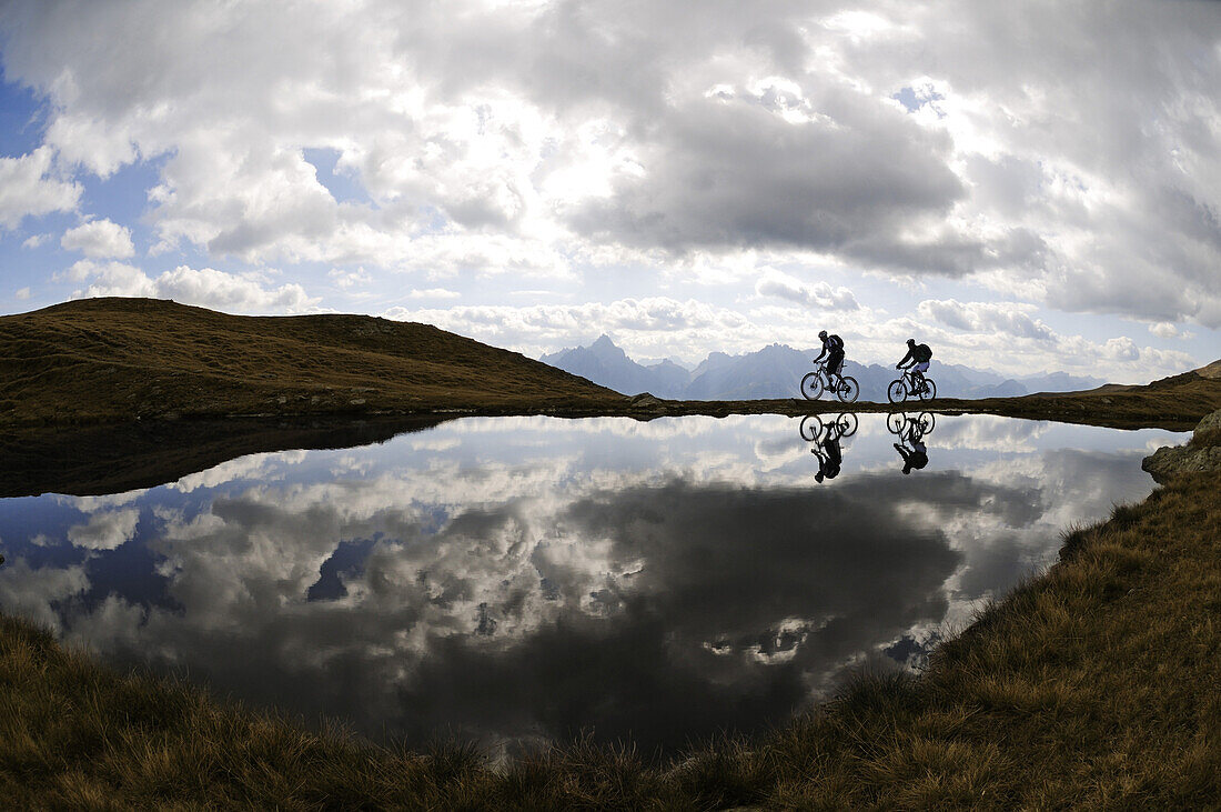 People on mountain bikes at mountain lake under clouded sky, Markinkele, Innichen, Val Pusteria, Dolomites, South Tyrol, Italy, Europe