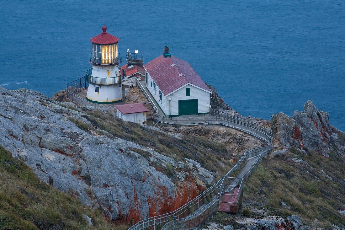 USA, California, Marin County, Point Reyes National Seashore, old lighthouse on the left, modern light on the right, perched on a point of Point Reyes conglomerate rock with red lichen, staircase and resting platform for visitors, dusk