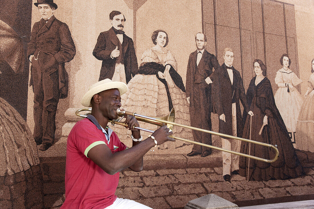Trombone player in a street with mural painting in background in the Historic District of Havana, Cuba