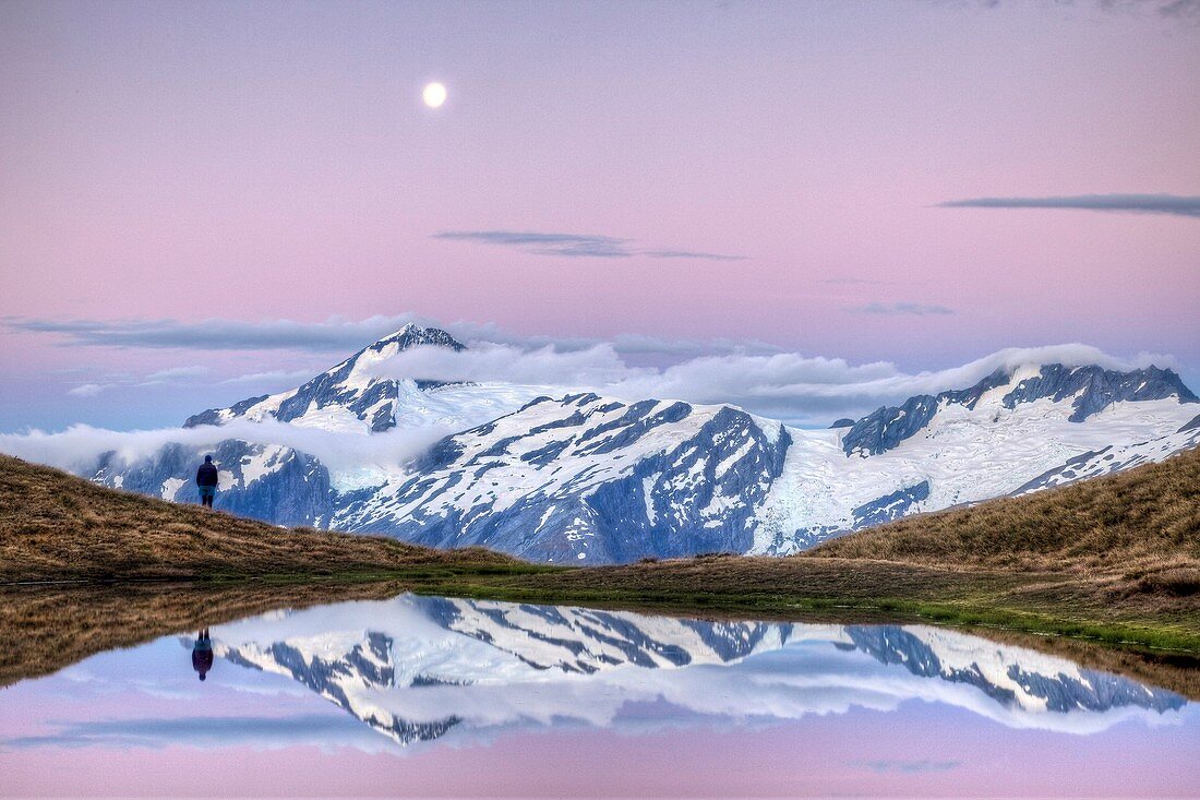 Mt Aspiring, tramper enjoys moonrise at dusk, Cascade saddle tarn, Mount Aspiring National Park, Otago, New Zealand