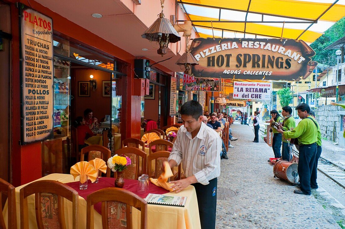 An outdoor restuarant with colorful table setting and entertainers in Agua Calientes, Peru