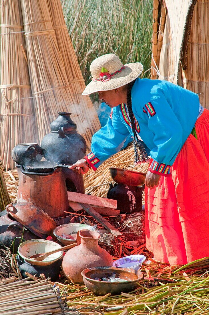 A woman in traditional dress cooking a meal on the floating Islands in Lake Titicaca, Peru, South America