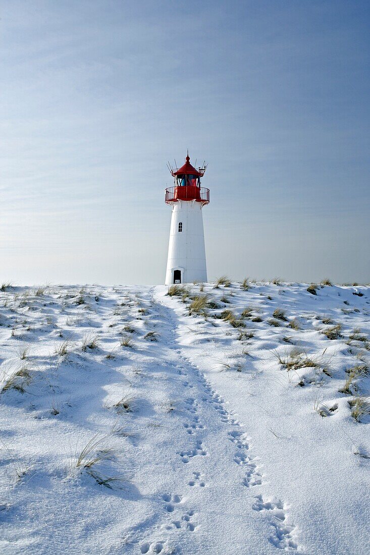 Lighthouse List West, seen from a low perspective, on snow covered dunes showing tracks of a rabbit leading to the lighthouse, with a bright blue sky at a sunny day, Sylt, Northfrisian Islands, Schleswig-Holstein, Northern Germany, Europe