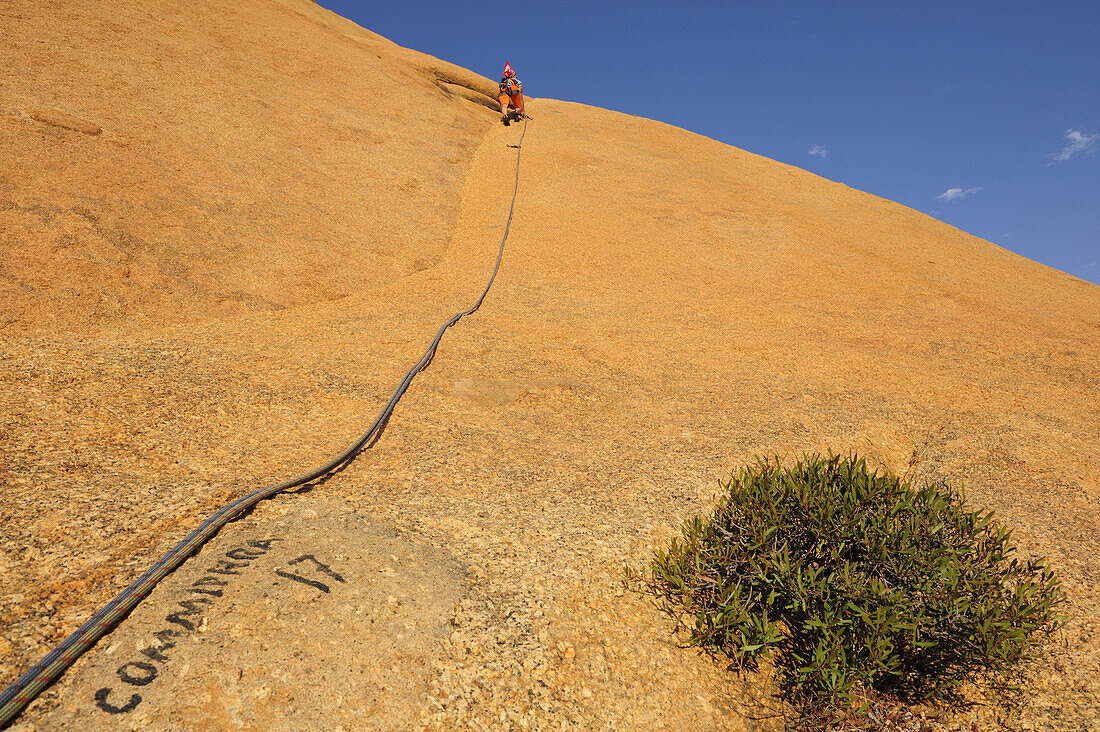 Frau klettert an roter Felswand, Große Spitzkoppe, Namibia