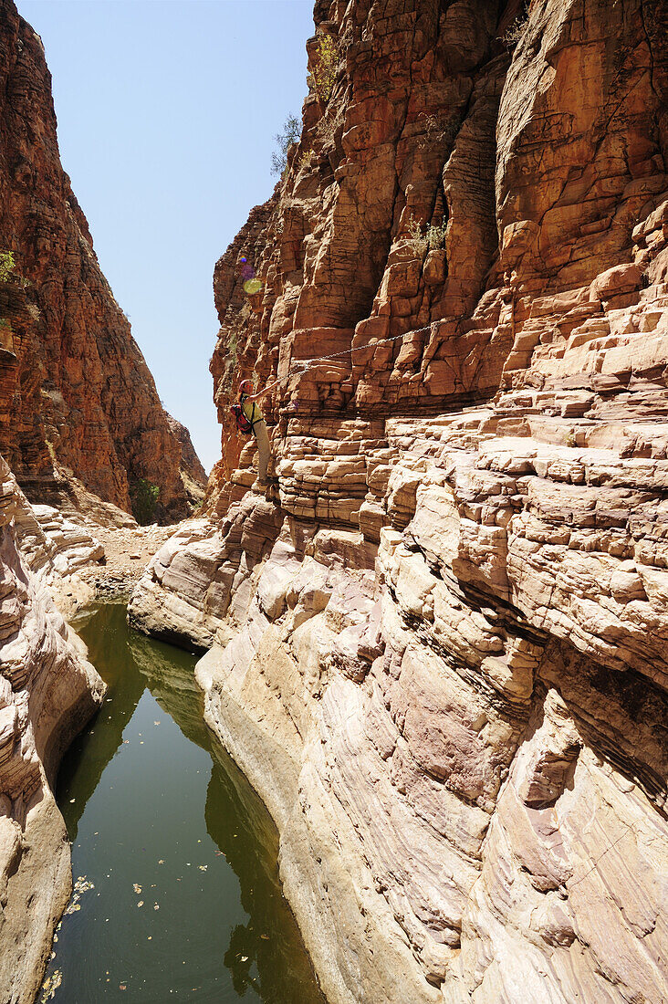 Woman crossing canyon with waterpool at chain, Olive trail, Naukluft mountains, Namib Naucluft National Park, Namibia