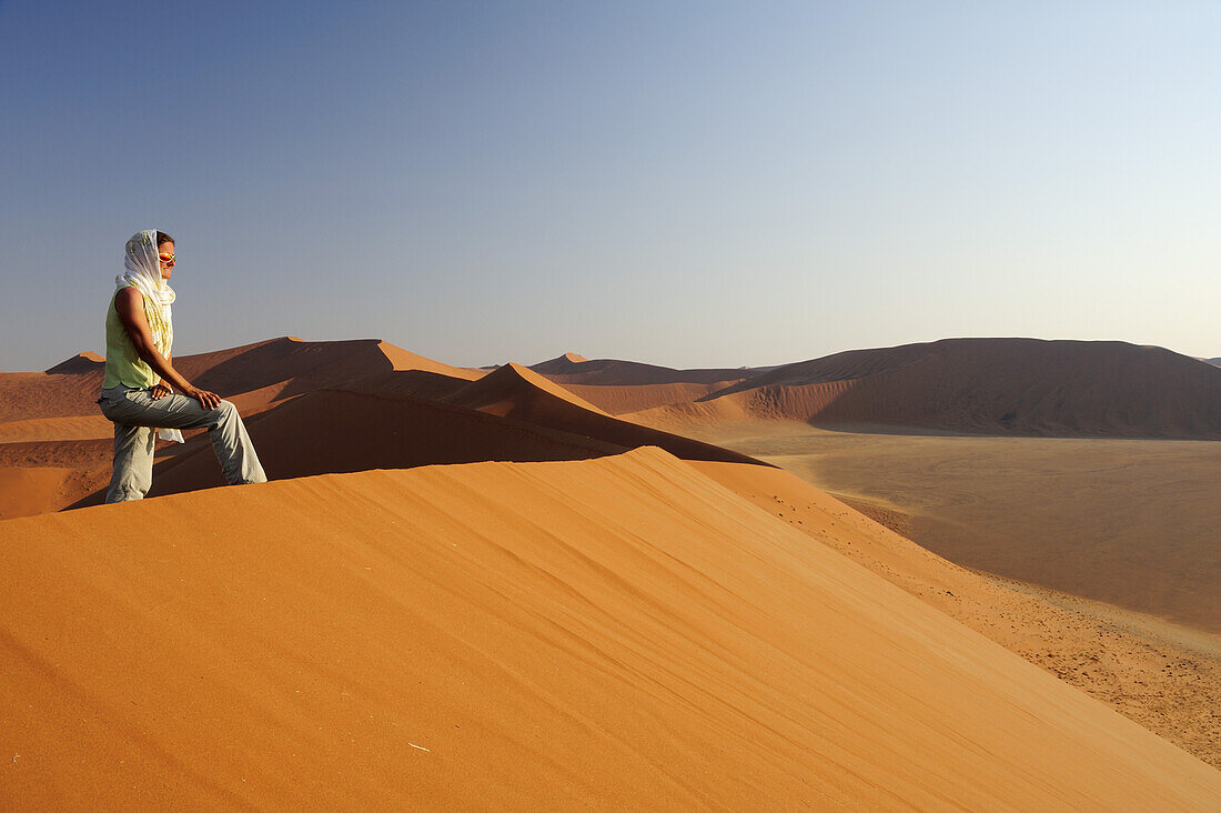 Frau steht auf roter Sanddüne und genießt Aussicht im Sossusvlei, Düne 45, Sossusvlei, Namib Naukluft National Park, Namibwüste, Namib, Namibia