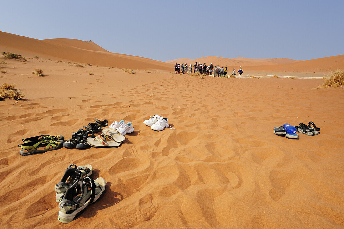 Several pairs of shoe in red sand, group of people in background, Sossusvlei, Namib Naukluft National Park, Namib desert, Namib, Namibia