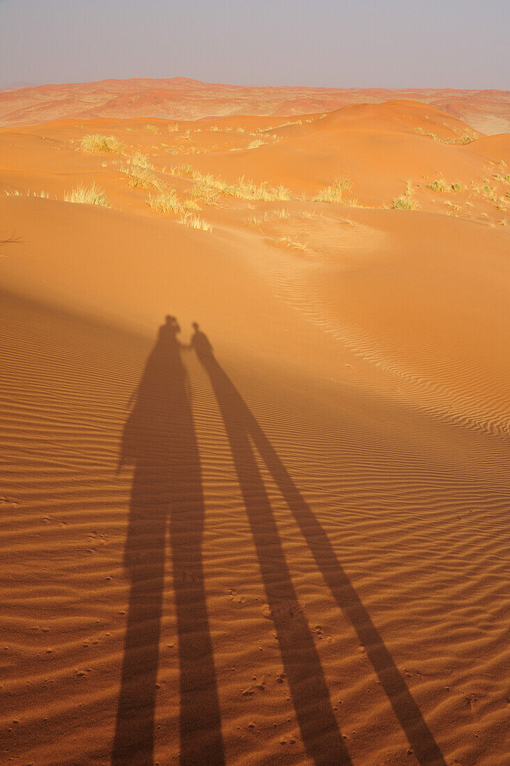 Two people holding hands throwing shadow on red sand dunes, Namib Rand Nature Reserve, Namib desert, Namib, Namibia