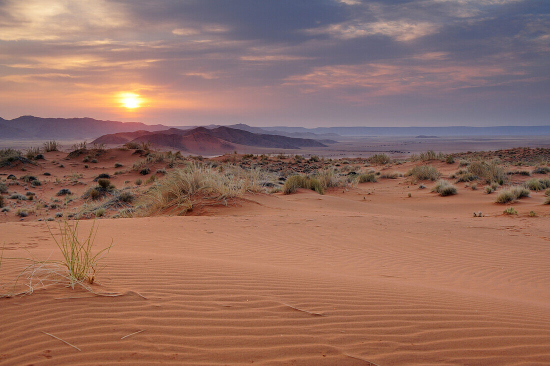 Sunrise over red sand dunes with Tiras mountains in background, Namib desert, Namibia