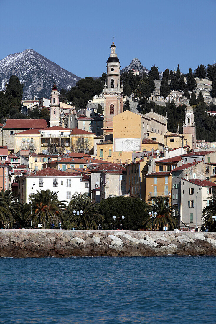 Colourful House Facades In The Old Town Of Menton And The Saint-Michel-Archange Basilica With Its Campanile In Front Of The Snow-Covered Mountains, Alpes-Maritimes (06), France