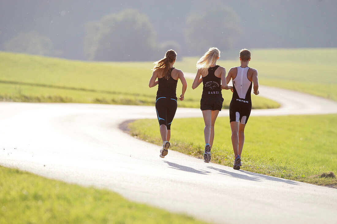 Three runners on road near Munsing, Upper Bavaria, Germany