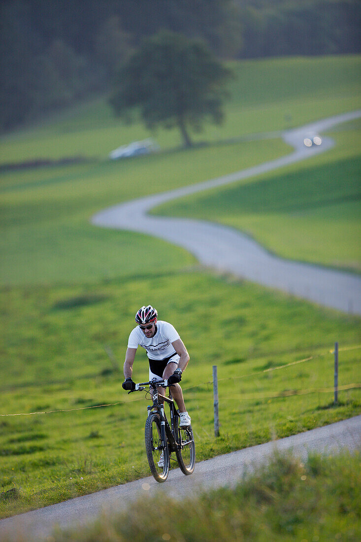 Mountainbiker auf einer Landstraße bei Münsing, Oberbayern, Deutschland