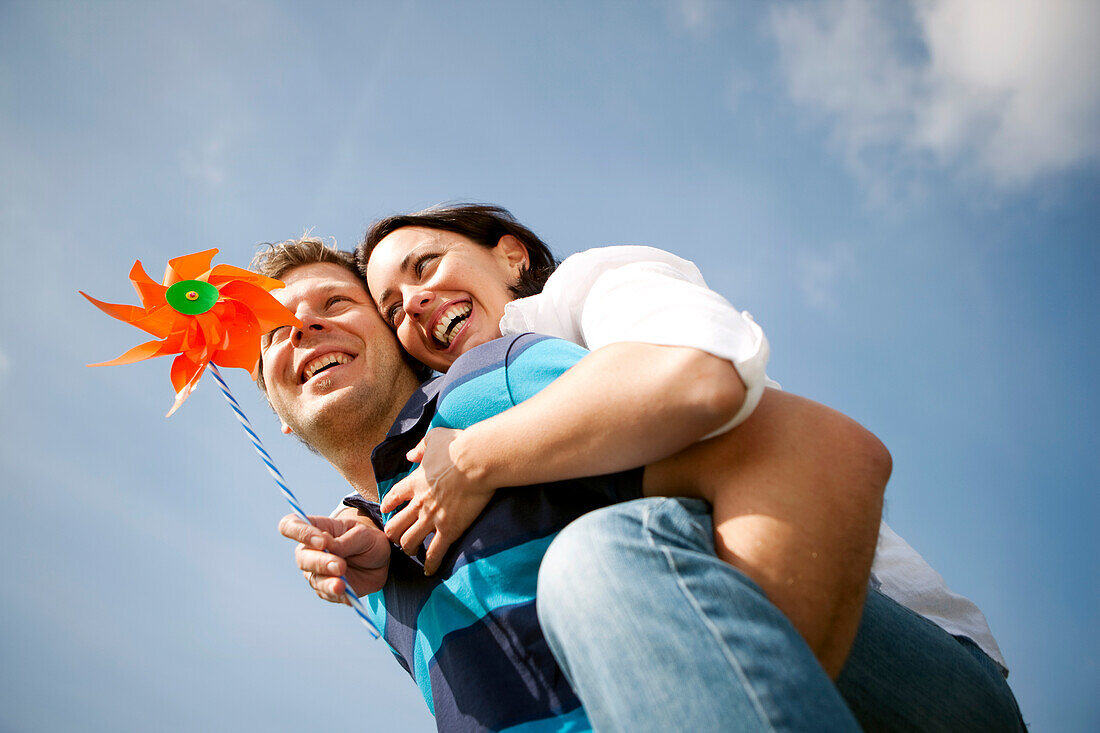 Mid adult man giving woman with pinwheel a piggyback ride