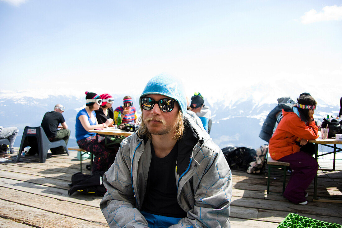 Mann mit Sonnenbrille sitzt auf einer Terrasse, Café No Name, Skigebiet Flims Laax Falera, Laax, Graubünden, Schweiz