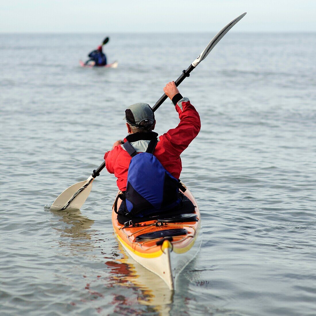rear view of two people paddling sea kayaks, UK