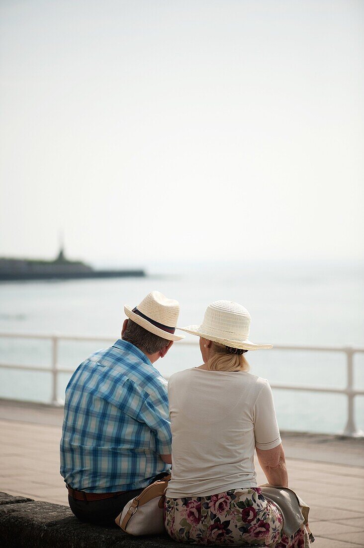 Rear view of an adult senior couple, man woman, sitting outside wearing hats, Summer afternoon, Aberystwyth Ceredigion wales UK