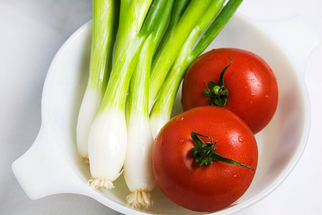 Spring onions and tomatoes in a white bowl on a white background