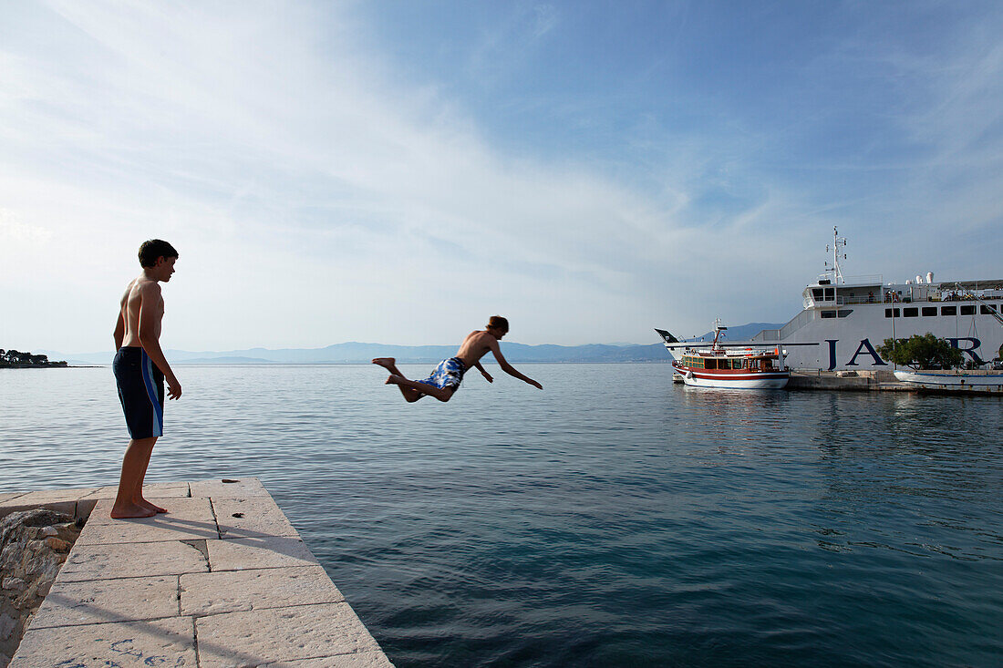 Boy jumping into water at harbor, Supetar, Brac, Split-Dalmatia, Croatia