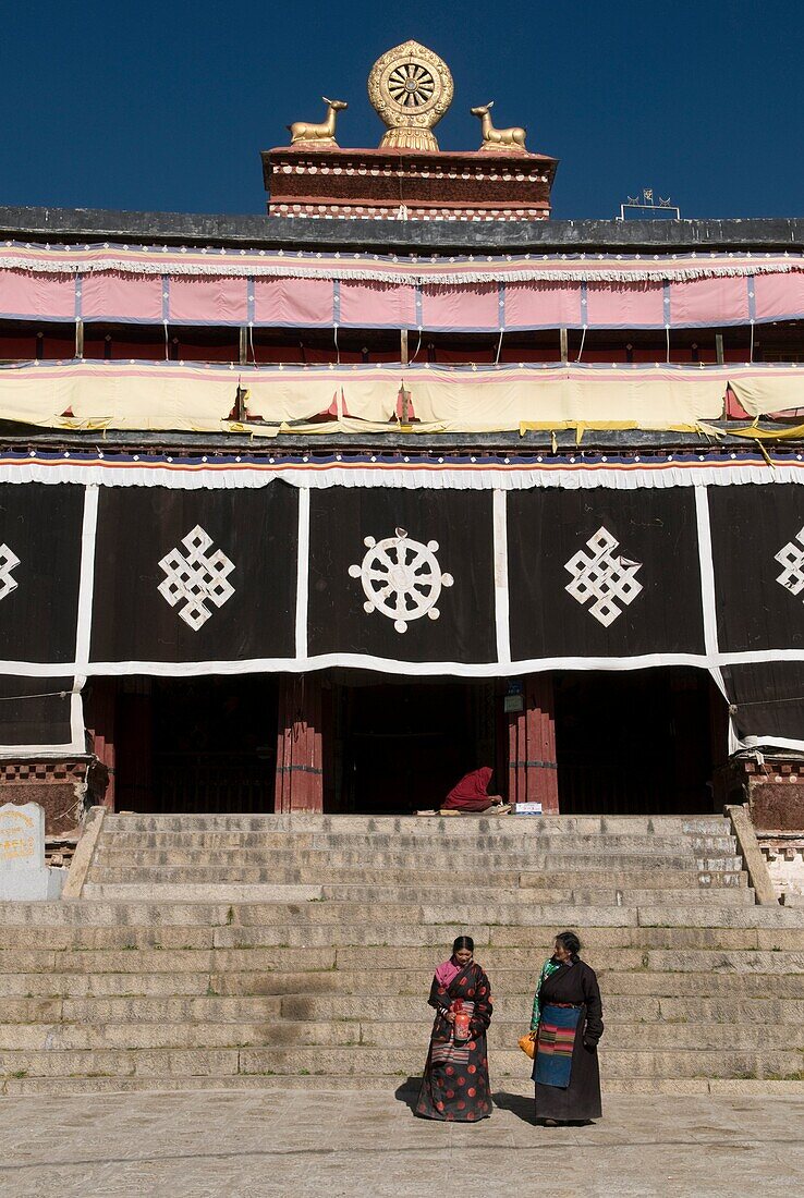 Two women wearing traditional Tibet dress in front of the main prayer hall at the famous Drepung Monastery, the largest in Lhasa Tibet
