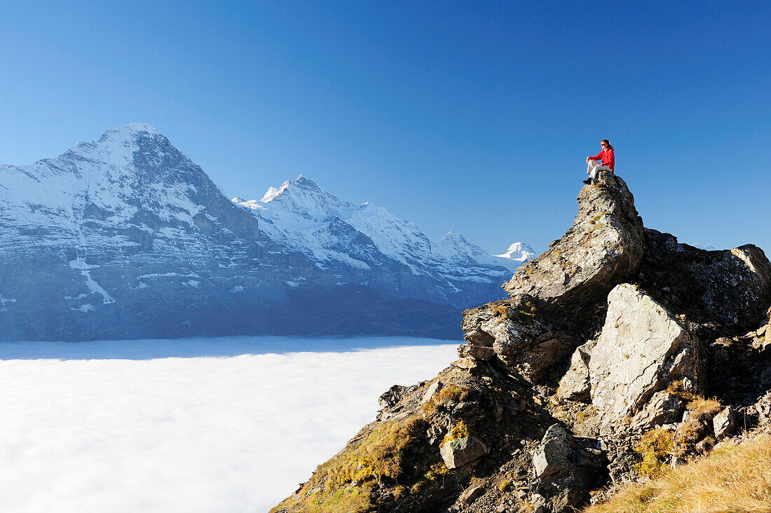 Frau sitzt auf Felsen und blickt auf Eiger und Jungfrau über Nebelmeer, Bussalp, Grindelwald, UNESCO Welterbe Schweizer Alpen Jungfrau - Aletsch, Berner Oberland, Bern, Schweiz, Europa