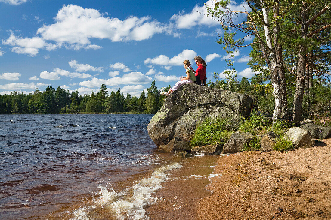 Mother and daughter sitting on a rock at lake Store Hindsjon, Kalmar county, Smaland, Sweden