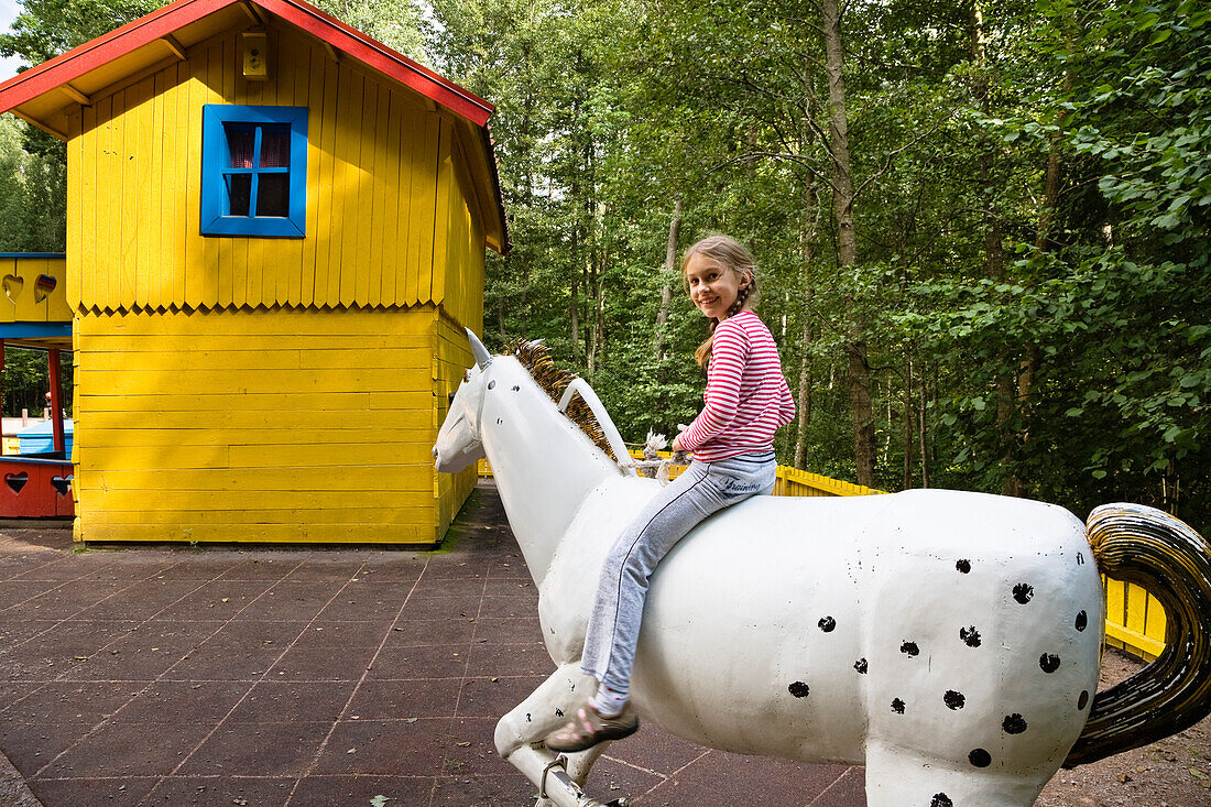 Girl sitting on a wooden horse, Astrid Lindgren Värld, Astrid Lindgren World, Vimmerby, Smaland, South Sweden, Europe