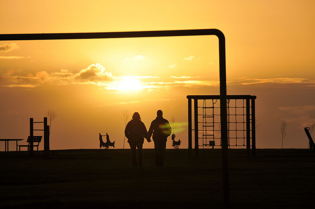 Couple walking hand in hand at sunset near the coast, Spieka near Nordholz, North Sea coast of Lower Saxony, Germany