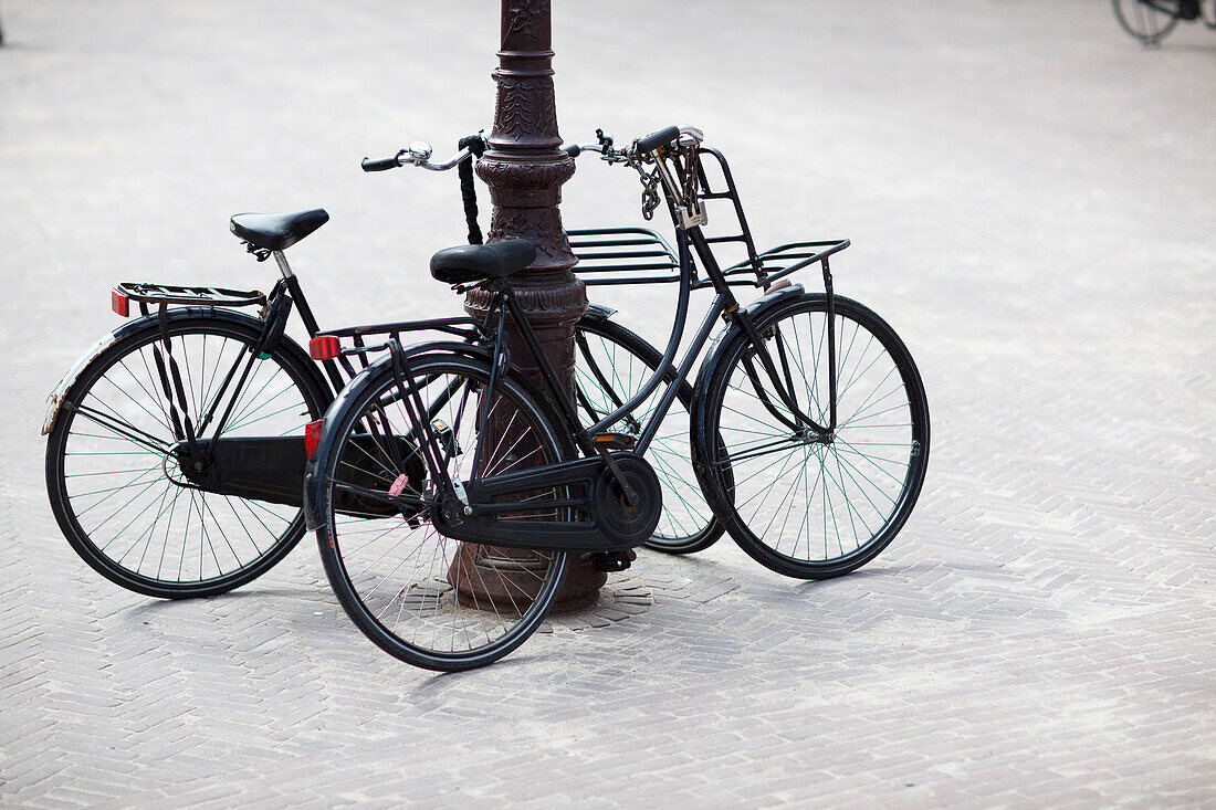 Two dutch bicyles, upright bicycles leaning against a lamppost, Amsterdam, Netherlands