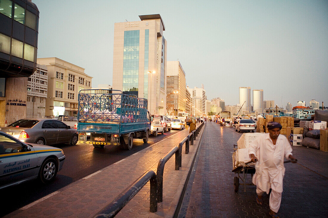 Orientalischer Mann mit Handwagen an befahrener Strasse, Dubai, Vereinigte Arabische Emirate