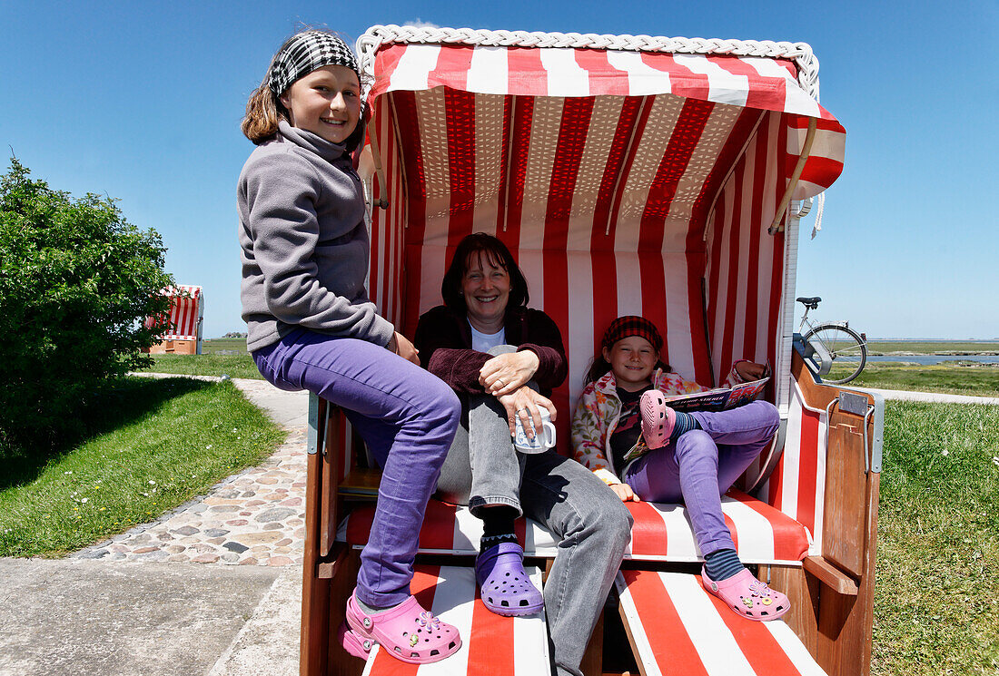 Mother and two daughters sat on a canopied beach chair on the Lorenzwarft, Hallig Hooge, North Sea, Schleswig-Holstein, Germany
