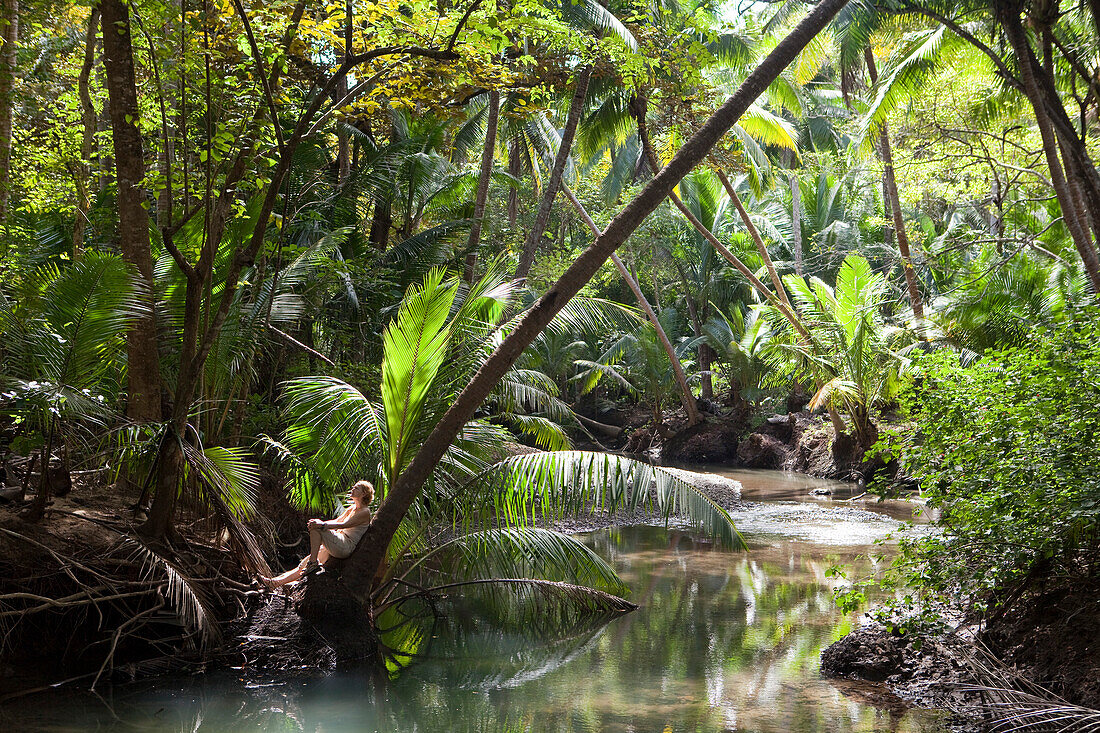 Frau enstpannt sich auf Palme am Ufer von einem Fluss in der Curu Nature Reserve, Curu, Puntarenas, Costa Rica, Mittelamerika, Amerika