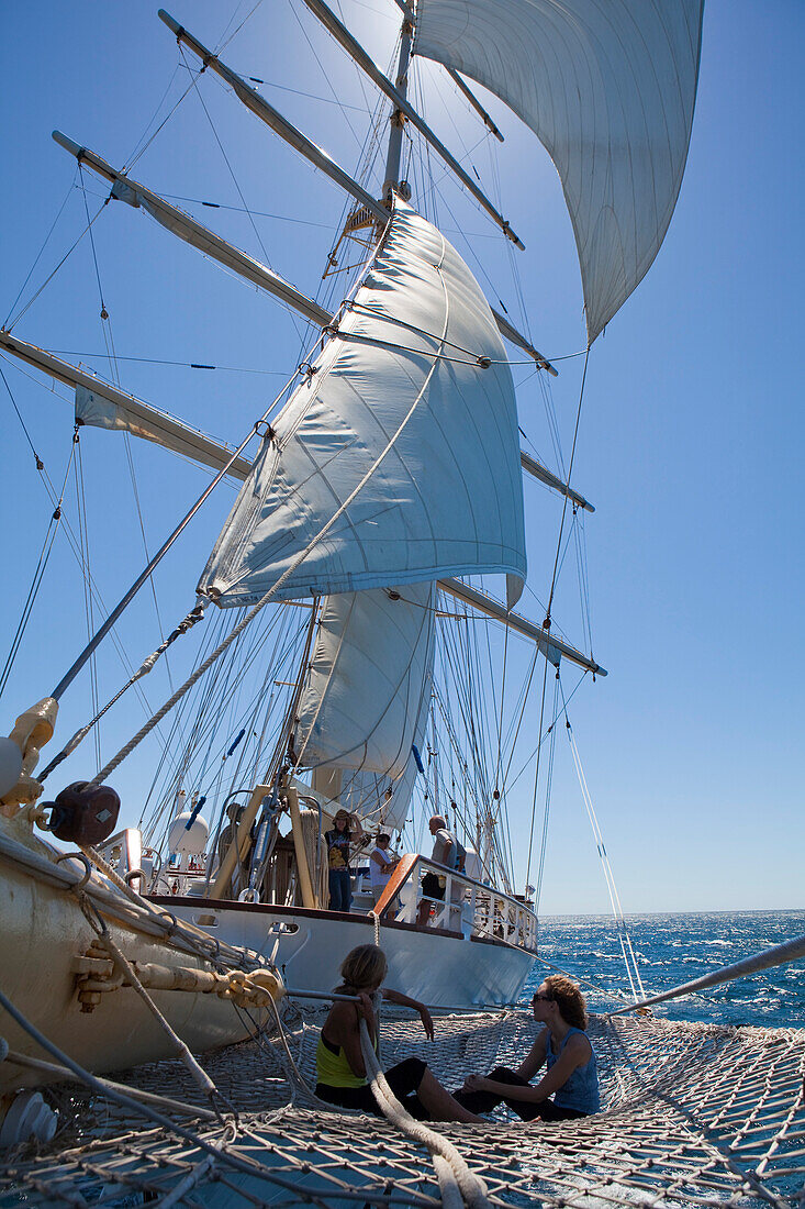 People relax on bowsprit net of sailing cruiseship Star Flyer (Star Clippers Cruises), Pacific Ocean, near Costa Rica, Central America, America