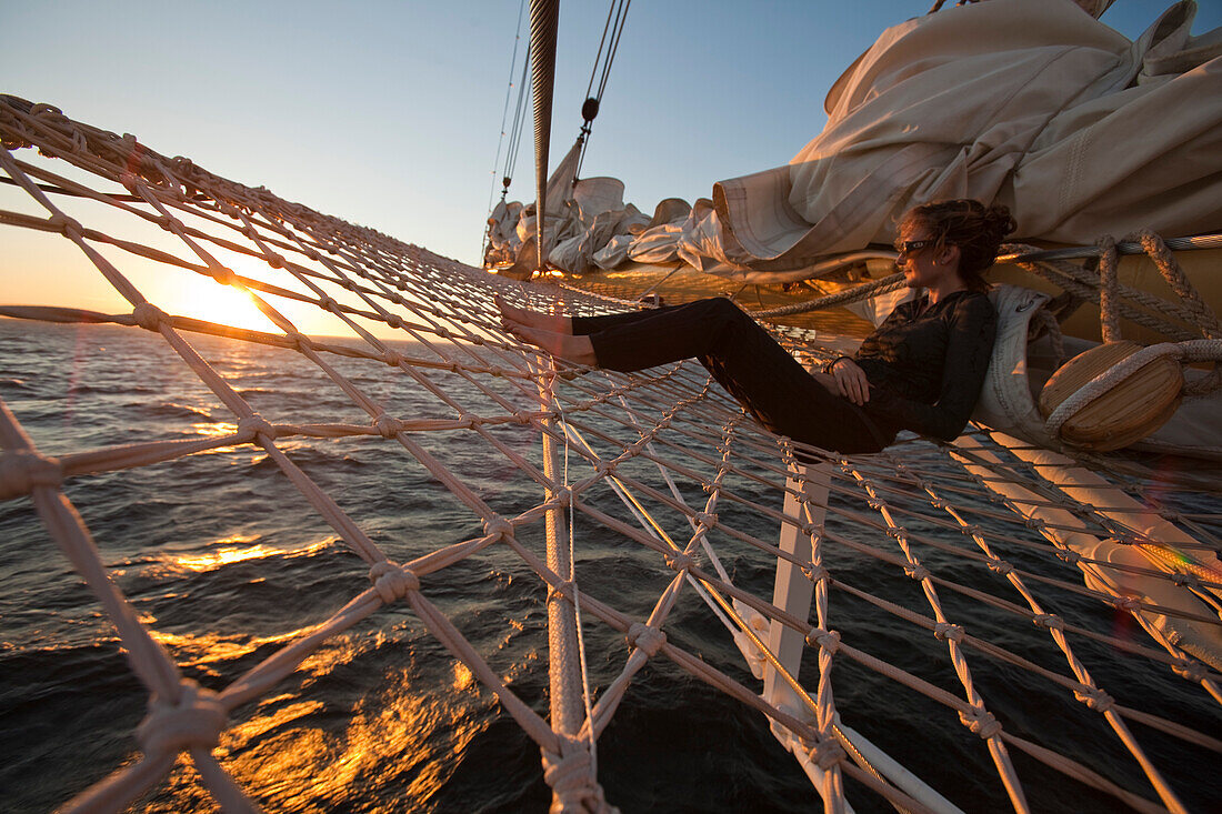 Junge Frau entspannt sich im Netz am Bugspriet vom Großsegler Kreuzfahrtschiff Star Flyer (Star Clippers Cruises) bei Sonnenuntergang, Pazifischer Ozean nahe Costa Rica, Mittelamerika, Amerika