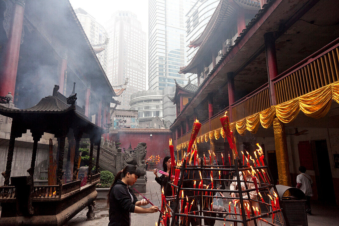 Frauen zünden Kerze an, Luohan Tempel, buddhistischer Tempel im Stadtzentrum, Hochhäuser und Wohnhäuser im Hintergrund, Chongqing, VR China