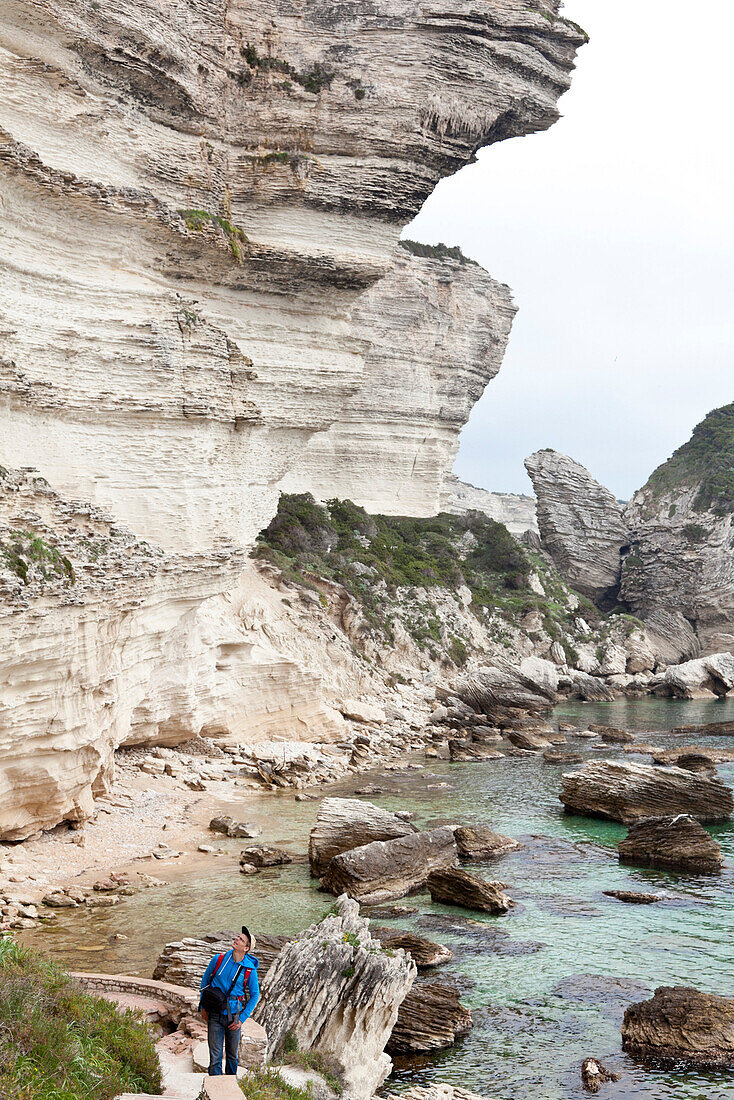Coastal landscape at the foot of Bonifacio, tourist on rocks looking upwards, village of Bonifacio is situated on the top of cliffs above the sea, Bonifacio, Corsica, France