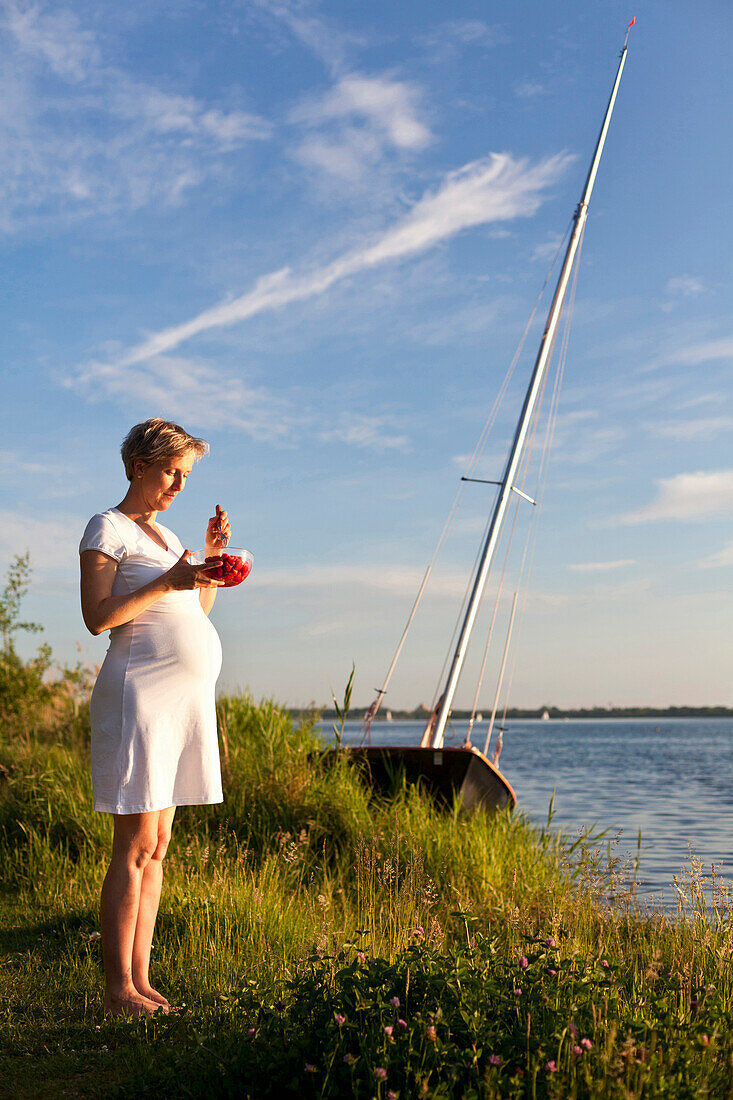 Pregnant woman eating strawberries near Cospuden Lake, Leipzig, Saxony, Germany