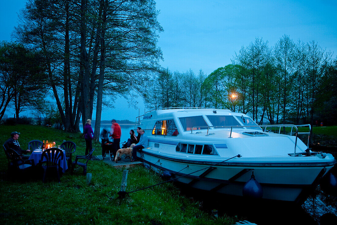 Menschen grillen neben Le Boat Hausbooten am Ufer vom Ellbogensee, nahe Fürstenberg/Havel, Mecklenburgische Seenplatte, Mecklenburg, Deutschland, Europa