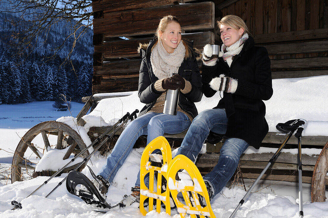 Two young women with snow shoe resting and drinking tea, valley of Leitzachtal, Upper Bavaria, Bavaria, Germany, Europe