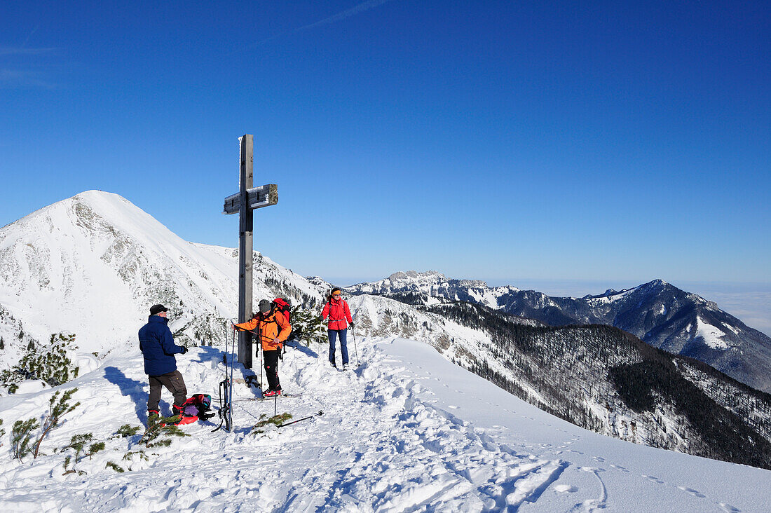 Skitourengeher stehen am Gipfelkreuz des Breitenstein, Geigelstein und Kampenwand im Hintergrund, Breitenstein, Chiemgauer Alpen, Chiemgau, Oberbayern, Bayern, Deutschland, Europa