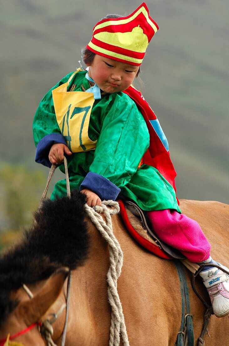 Four-year-old girl riding a horse, participant in the horsemanship competition of the Naadam Festival, Mongolia