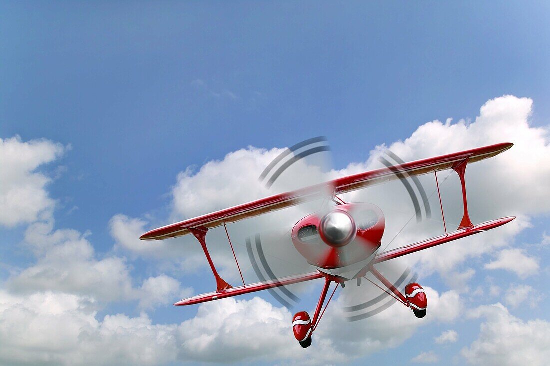 A red biplane flying in a blue cloudy sky