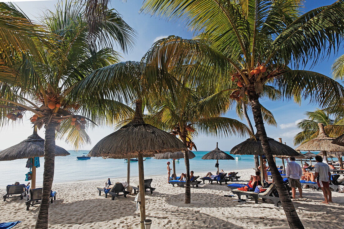 Palm trees and people on the beach of Beachcomber Hotel Paradis &amp; Golf Club, Mauritius, Africa